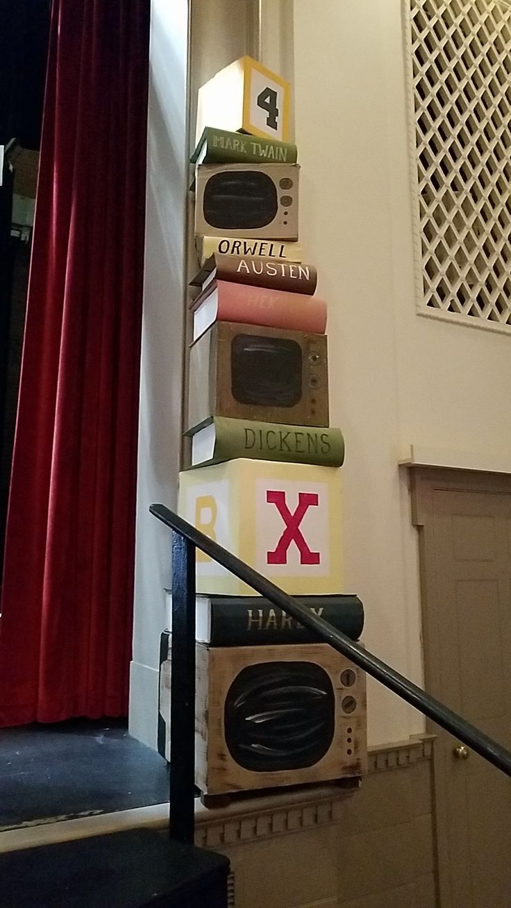 a stack of books sitting on top of a stair case next to a red curtain