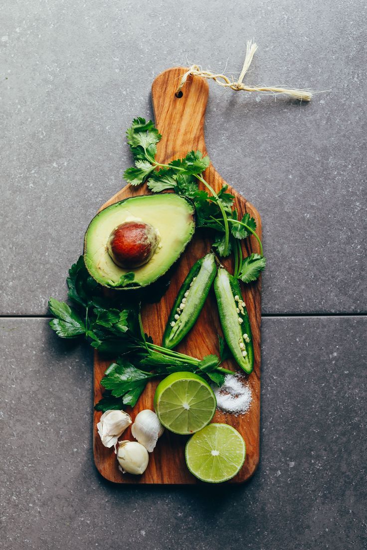 an avocado and other vegetables are on a cutting board with limes, cilantro