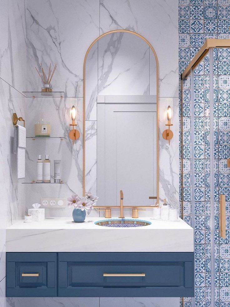 a bathroom with marble counter tops and blue cabinets, along with a gold framed mirror