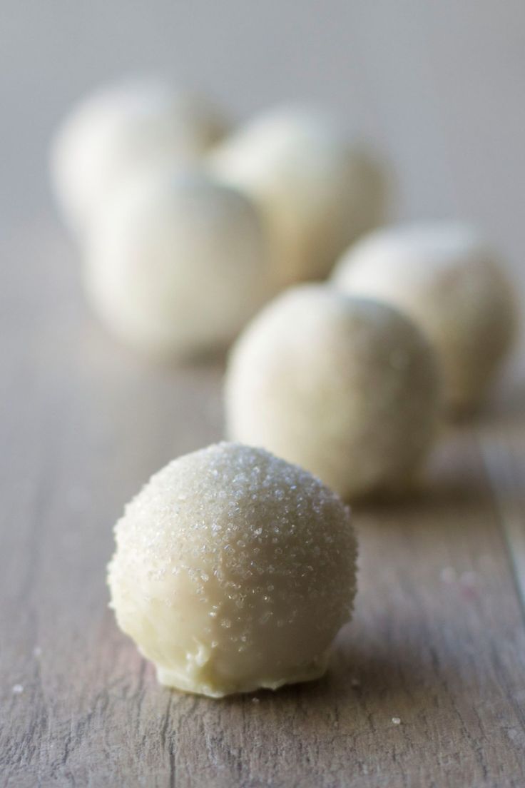 there are several balls of white chocolate on the wooden table and one is half covered in sugar