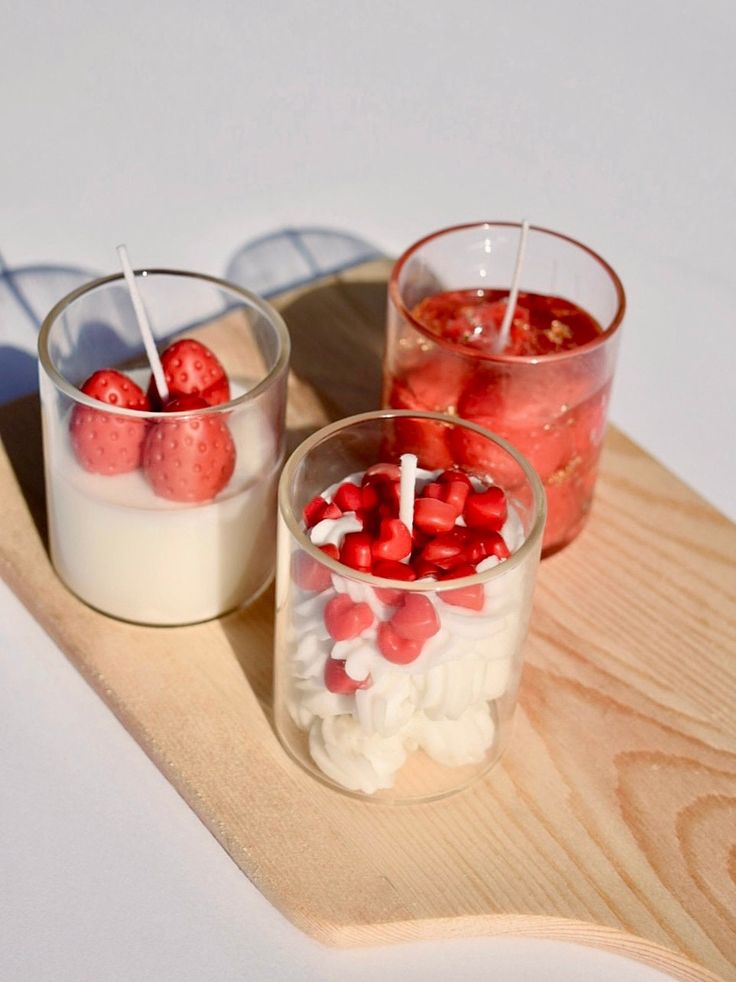 two candles with strawberries and marshmallows in them on a wooden tray