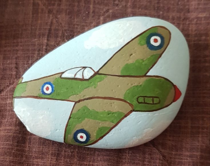 a painted rock with an airplane on it sitting on a brown cloth covered tablecloth