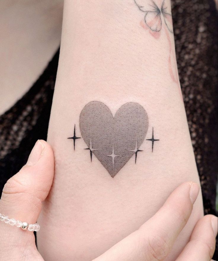 a woman holding her arm with a heart tattoo on it