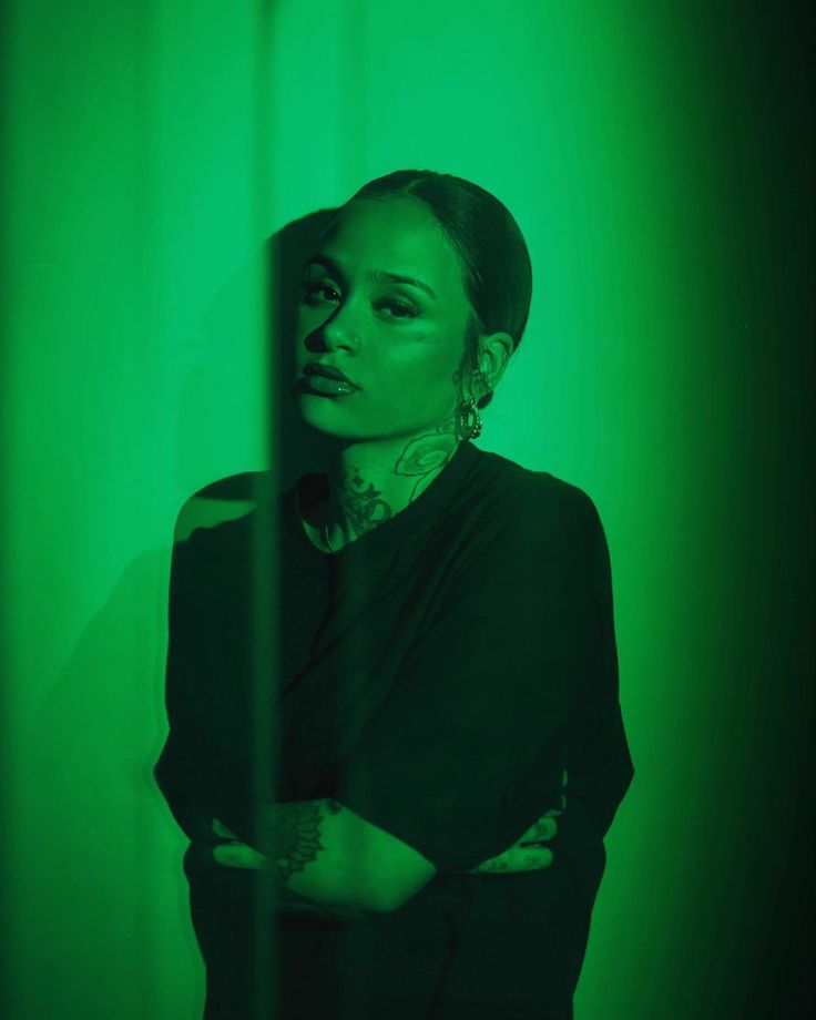 a woman standing in front of a green wall with her arms crossed and looking at the camera