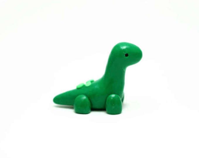 a green toy dinosaur sitting on top of a white surface