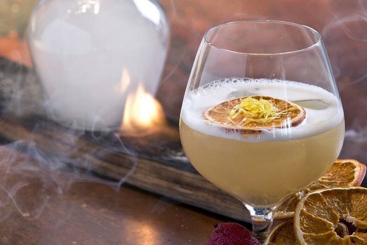 a glass filled with liquid sitting on top of a table next to sliced oranges and raspberries