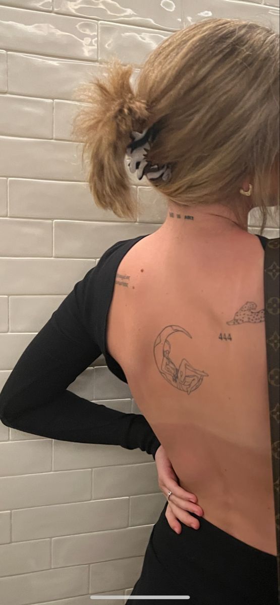 a woman with tattoos on her back standing in front of a white brick wall and looking into the mirror