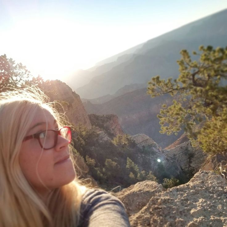 a woman taking a selfie on top of a mountain with the sun behind her