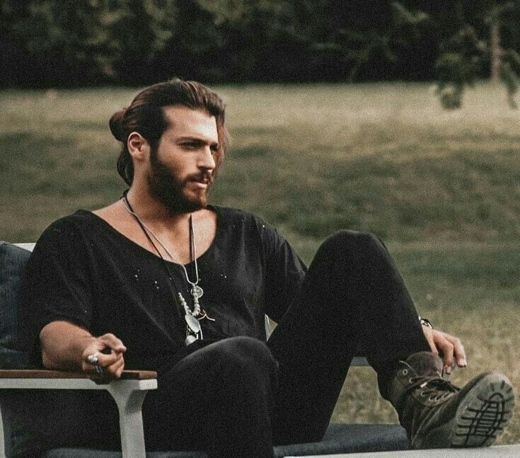 a man sitting on top of a white chair next to a tree and grass covered field