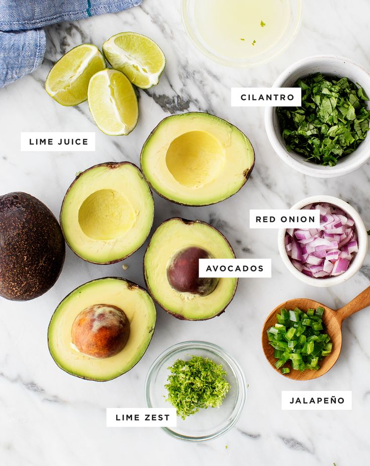 the ingredients for an avocado salad laid out on a marble counter