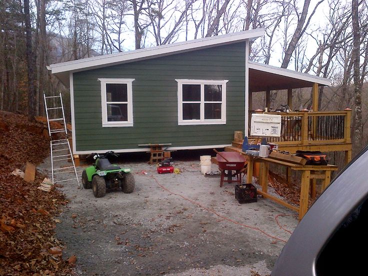 a small green house in the woods with lots of furniture and tools on the ground