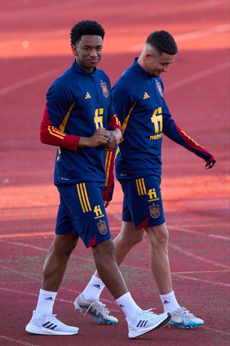 two soccer players are walking together on the field with their hands in each other's pockets