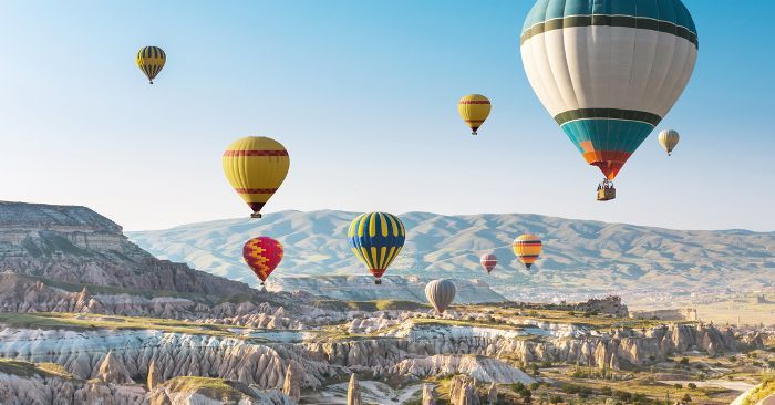 many hot air balloons are flying in the sky over some hills and valleys with trees