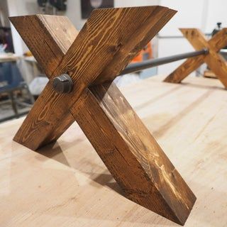 a wooden table topped with metal legs and an x design on top of the table