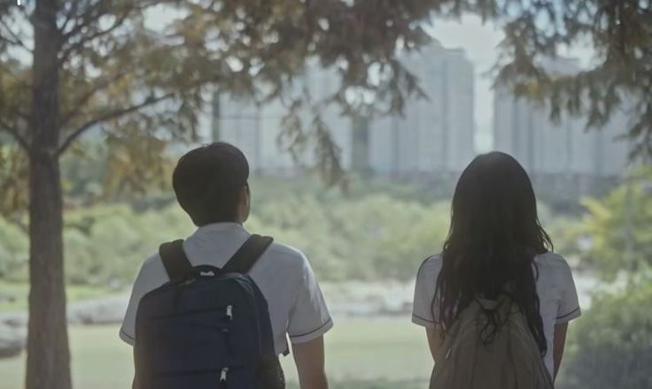 two young people are walking in the park with their backpacks on and one is looking back