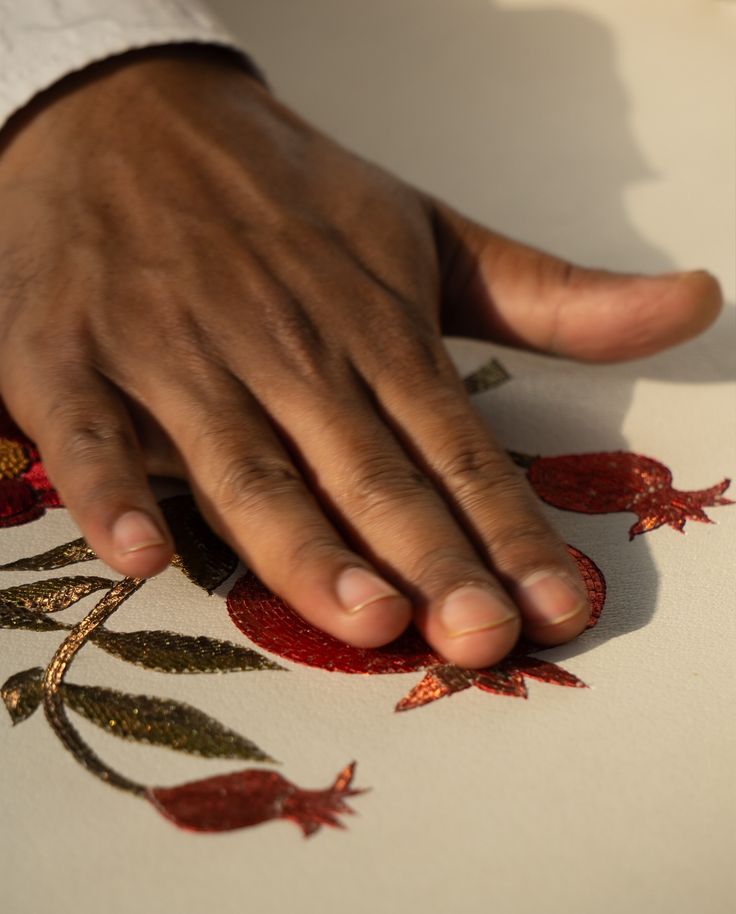 a person's hand on top of a piece of paper with red and green designs