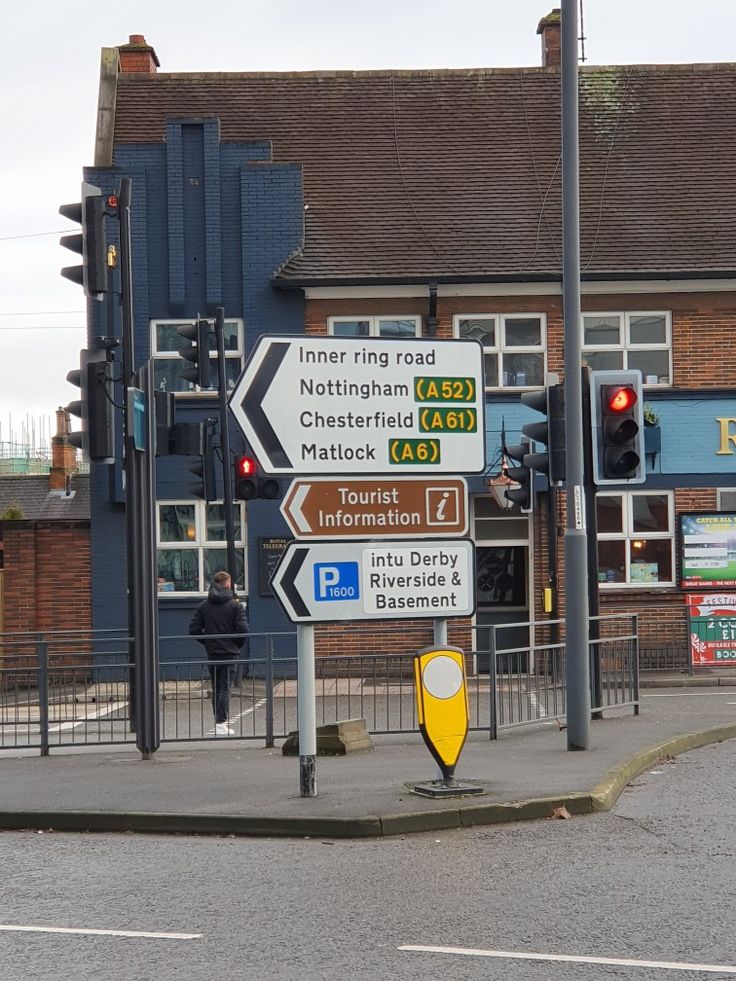 street signs in front of a building on a corner with traffic lights and people walking by