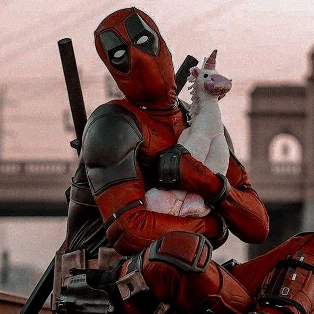 a man dressed as deadpool holding a stuffed animal in his arms and sitting on the ground