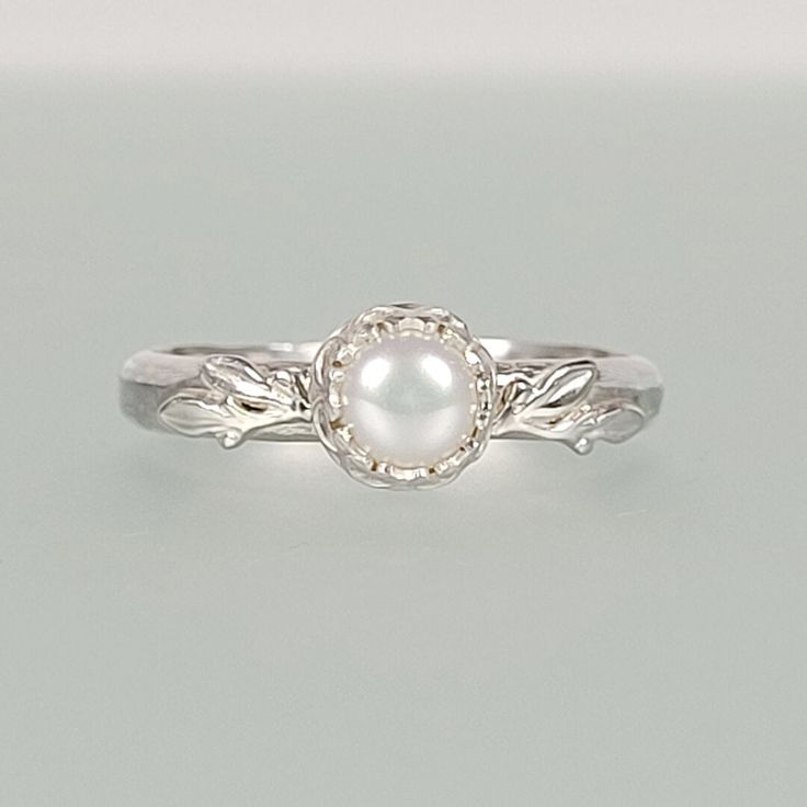 a white pearl sits on top of a silver ring with leaves in the middle and an oval