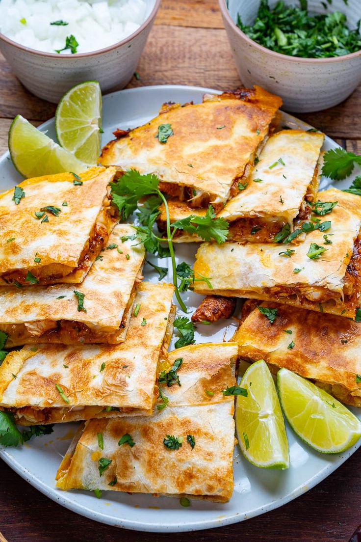 several quesadillas on a plate with limes and sour cream in the background