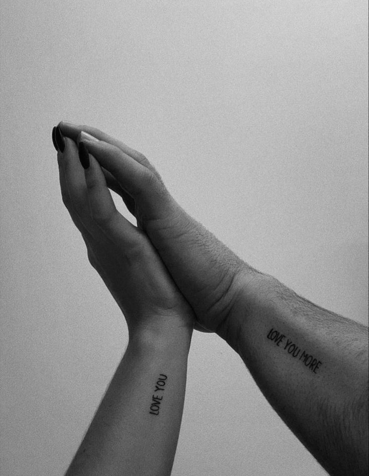 two people holding each other's hands with the words love you more tattooed on their arms