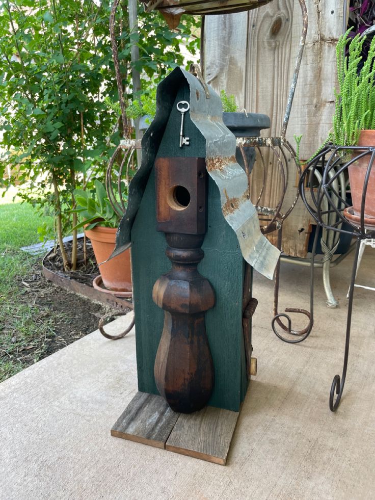 a birdhouse made out of wood sitting on top of a wooden pallet next to some potted plants