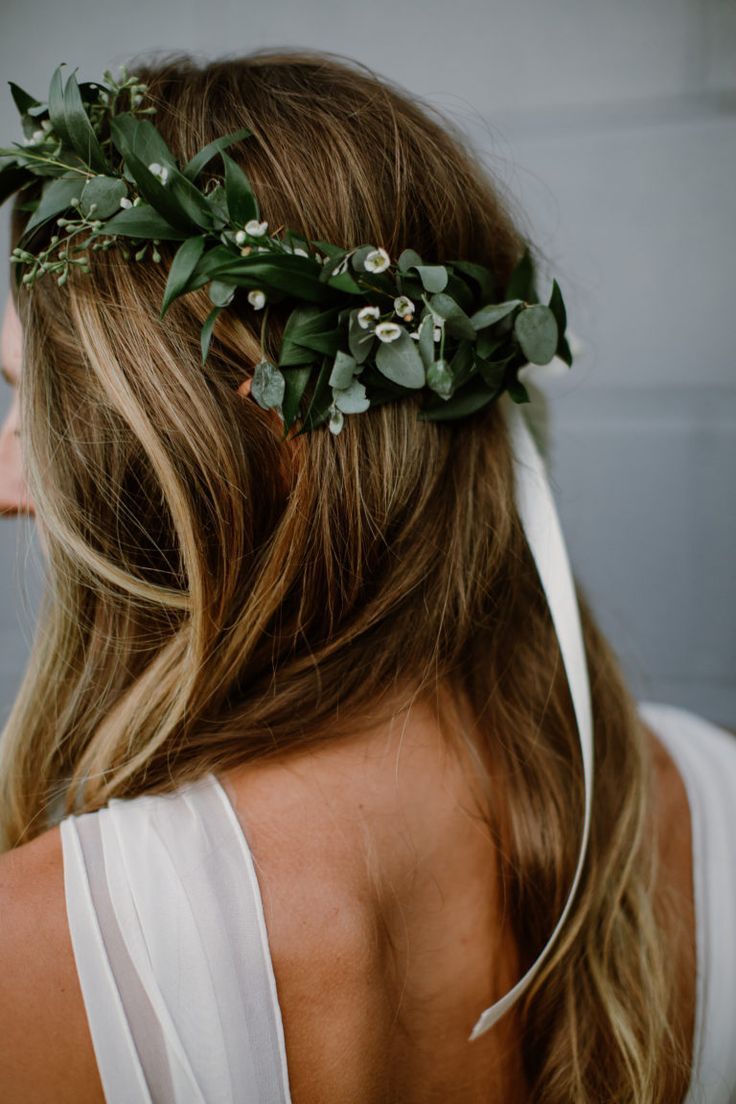 a woman wearing a flower crown with greenery on her head and white dress in the background