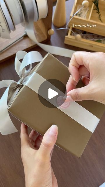 a person opening a brown gift box with a white ribbon