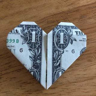 an origami heart made out of money on a wooden table with one dollar bill cut in half