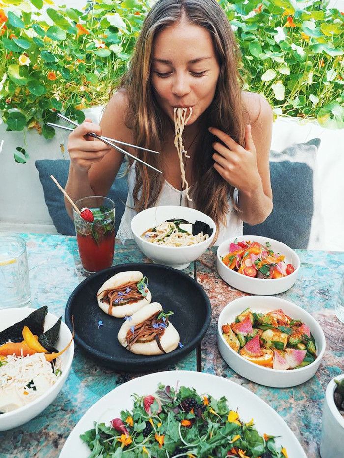 a woman sitting at a table eating food with chopsticks