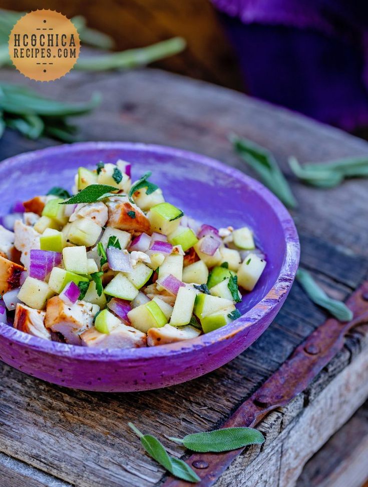 a purple bowl filled with food sitting on top of a wooden table next to green leaves