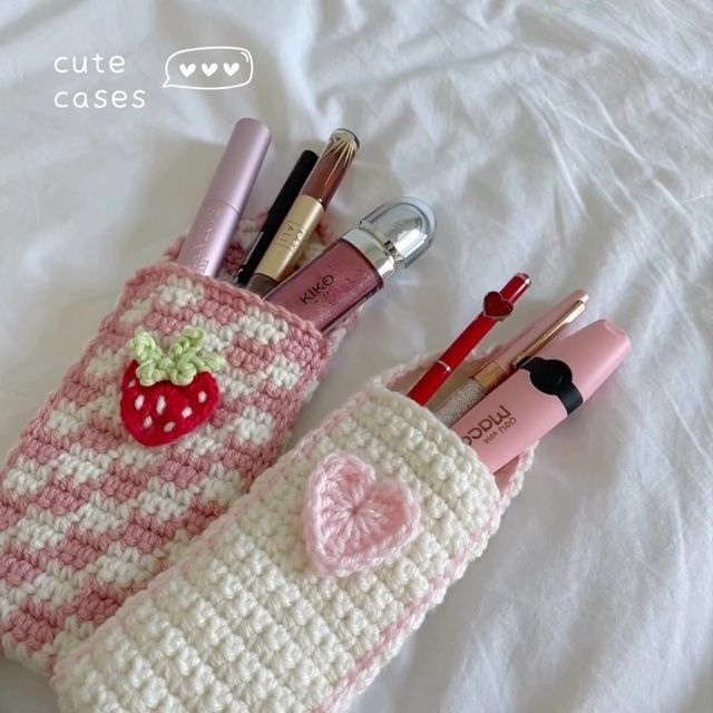 a crocheted bag with lipstick, pens and makeup brushes in it sitting on a bed