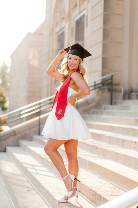 a woman in a graduation cap and gown posing on steps with her hand on her head