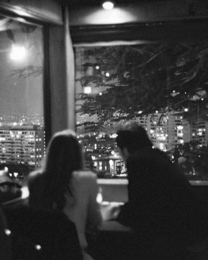 two people are sitting at a table in front of a window overlooking the city lights