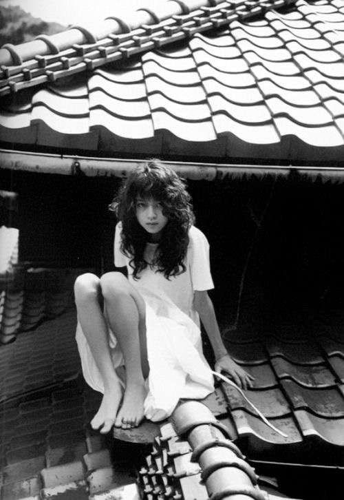 a woman sitting on the roof of a building with her legs crossed and looking down