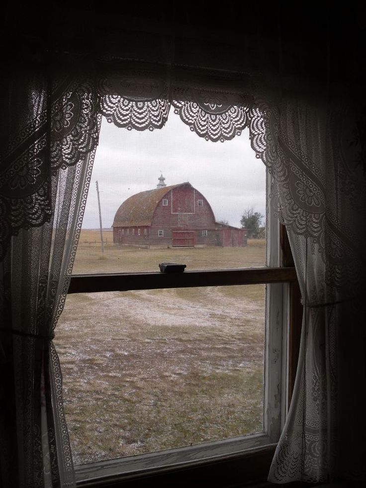 an open window looking out onto a field with a barn and silo in the distance