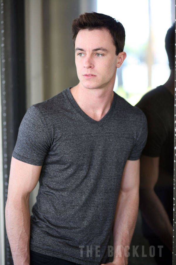 a man standing in front of a mirror wearing a gray shirt and black pants with his hands in his pockets