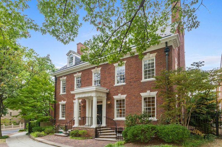 a large brick house in the middle of a street with lots of trees and bushes