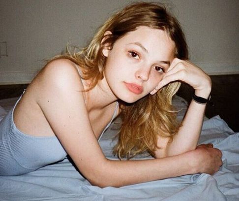 a young woman laying on top of a bed next to a white wall with her hand under her chin