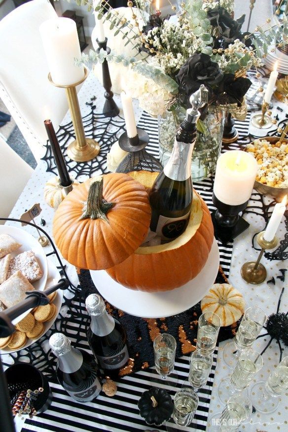 a table set for halloween with pumpkins, candles and wine bottles on it's centerpiece