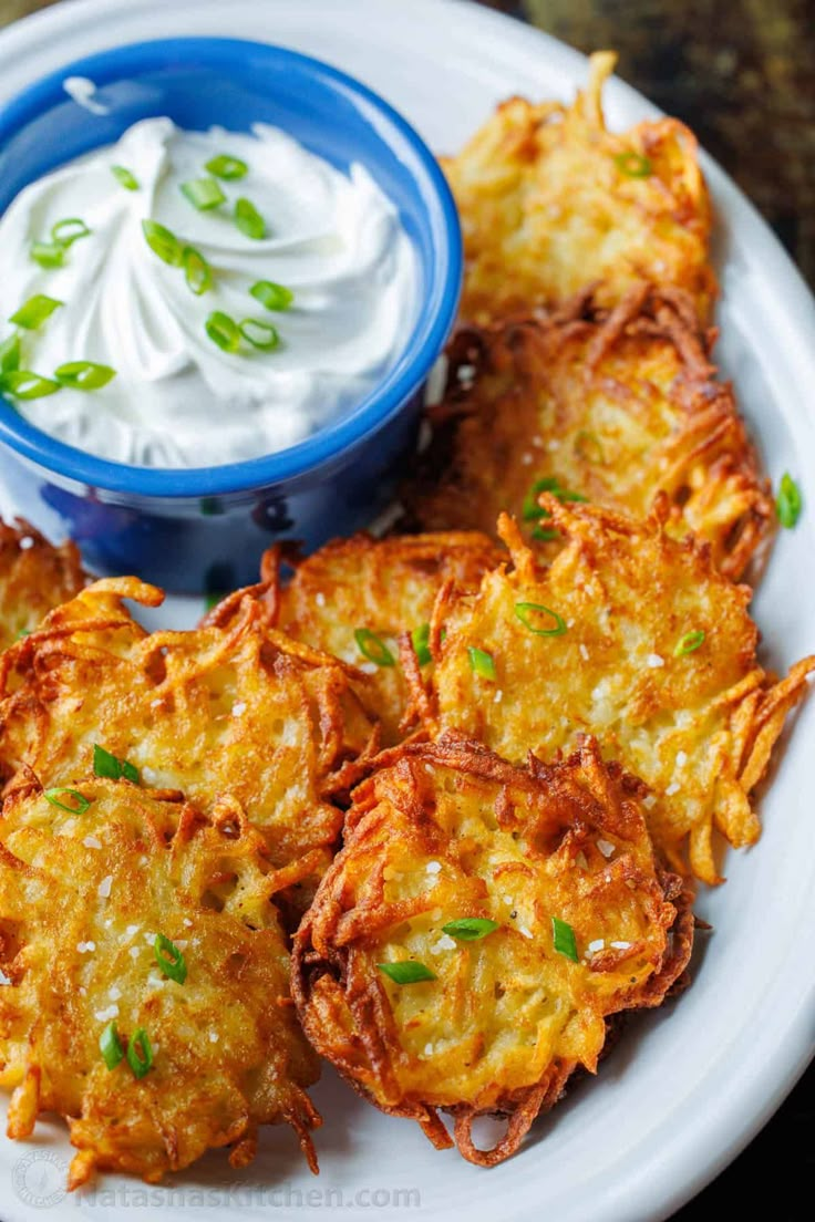 potato fritters with sour cream and chives on a white plate next to a blue bowl