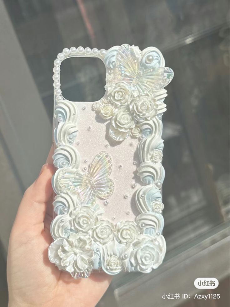 a hand holding up a phone case with flowers and butterflies on the back in front of a window