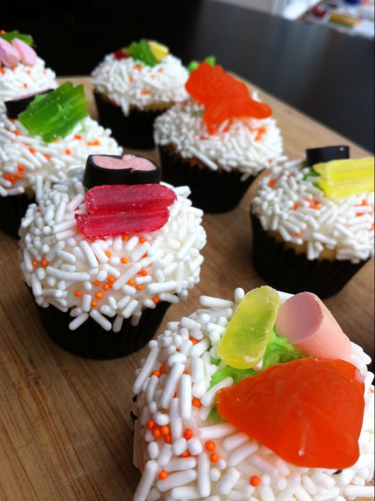 cupcakes with white frosting and colorful candies on top are arranged in the shape of hearts