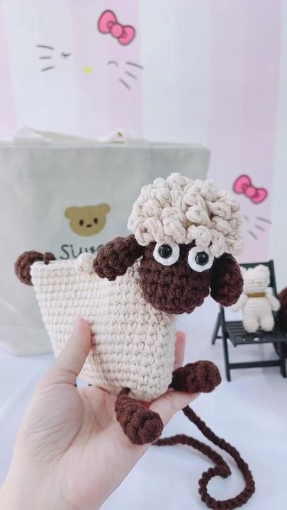 a hand holding a small crocheted sheep with big eyes and a brown tail