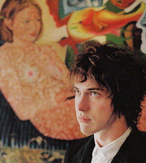 a man in a suit standing next to a wall with paintings on the walls behind him