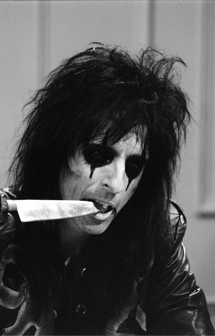 a man with black makeup holding a knife in his mouth