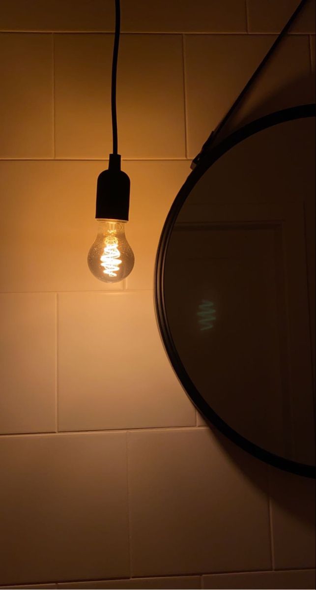 a light bulb is hanging from a wall next to a round mirror on a tiled wall