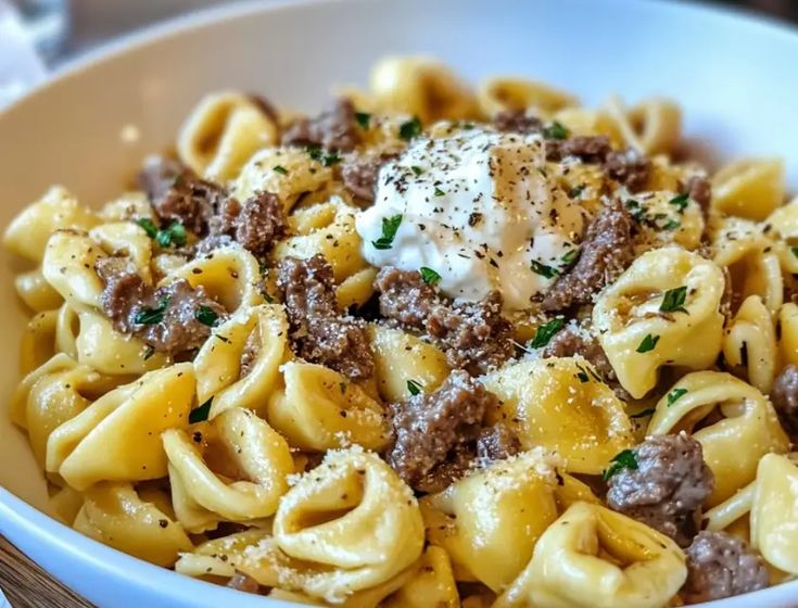 a close up of a bowl of pasta with meat and cheese on top, garnished with parsley