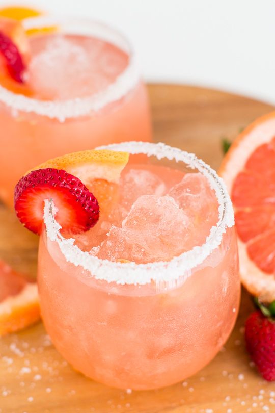 two glasses filled with pink lemonade and garnished with strawberries on a cutting board