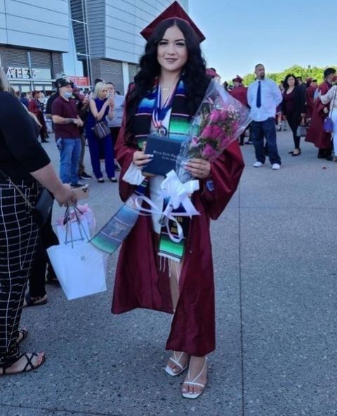 a woman wearing a graduation gown and holding flowers is standing in the middle of a crowd